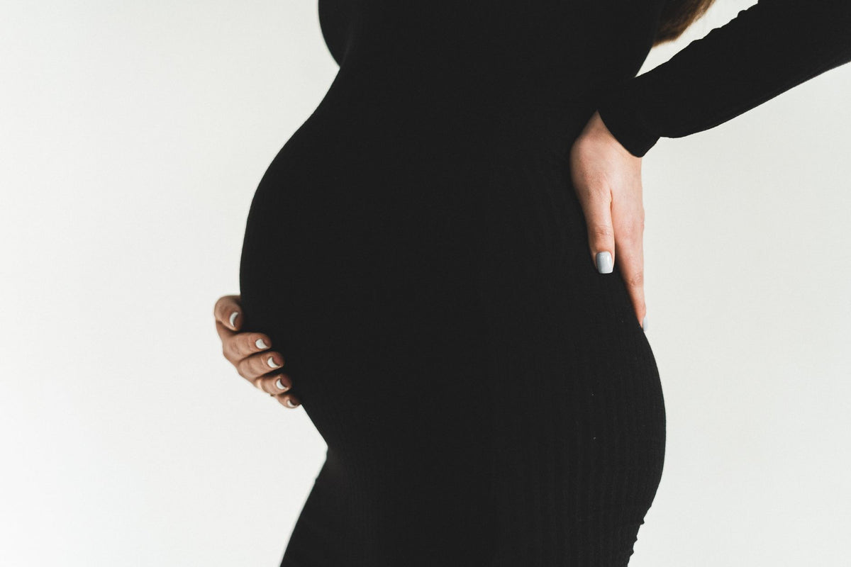 Close-up of a pregnant woman in a black dress holding her baby bump, symbolizing motherhood.